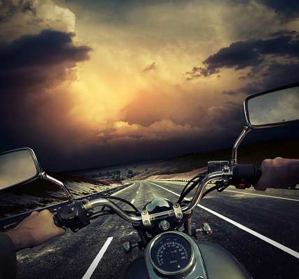 Rider on the motorcycle moving towards dark storm clouds on the asphalt road