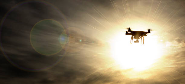 An Unmanned Aerial Vehicle, drone, in flight, silhouetted by the Sun.  