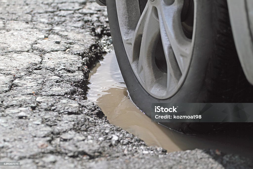 Alloy Wheel And Tire In A Pothole, Closeup Closeup shot of a vehicle slowly driving through a pothole, demonstrating the possible damage to tire and wheel. Shallow dof with focus on image centre. Pot Hole Stock Photo