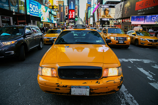 A black businesswoman with sunglasses in a plaid jacket and with a purse seen entering a yellow taxi in Manhattan during one busy day.