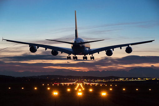 Photo of an airplane just before landing in the early morning. Runway lights can be seen in the foreground.