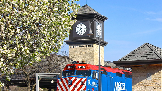 HIghland Park, IL, USA-May 7, 2015: A late springtime late afternoon view of a Metra train stopped at the Highland Park station, with clock tower and white tree blossoms.  