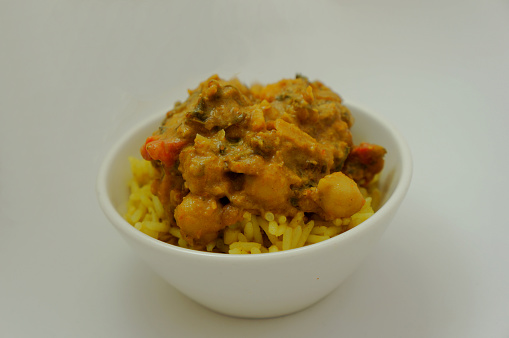 A vegetarian meal of spicy Indian Butternut Squash & Chickpea Curry served on a bed of yellow Pilau Rice in a white bowl