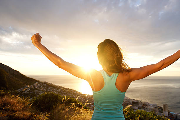 femme s'étirant les bras derrière de lever du soleil - arms outstretched arms raised women winning photos et images de collection