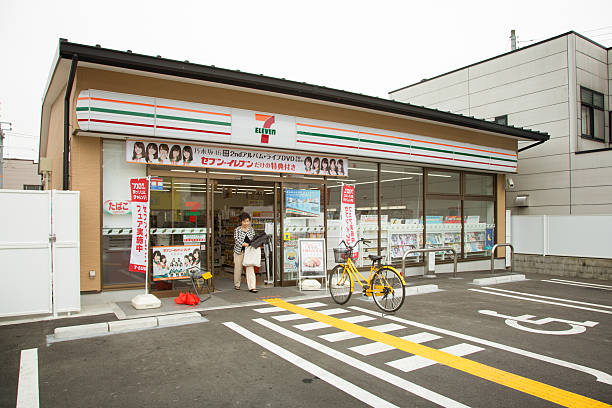 японский семь одиннадцать супермаркет с клиентом, гуляющих - franchising concepts brand name road sign стоковые фото и изображения