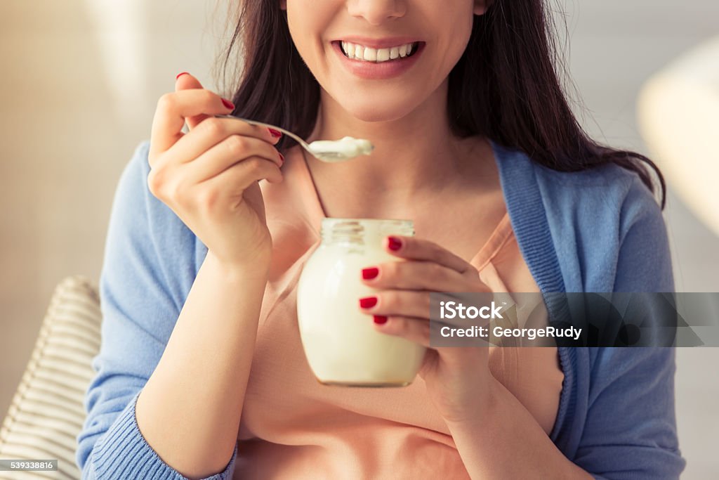 Beautiful pregnant woman Cropped image of beautiful pregnant woman eating yogurt and smiling while sitting at home Yogurt Stock Photo