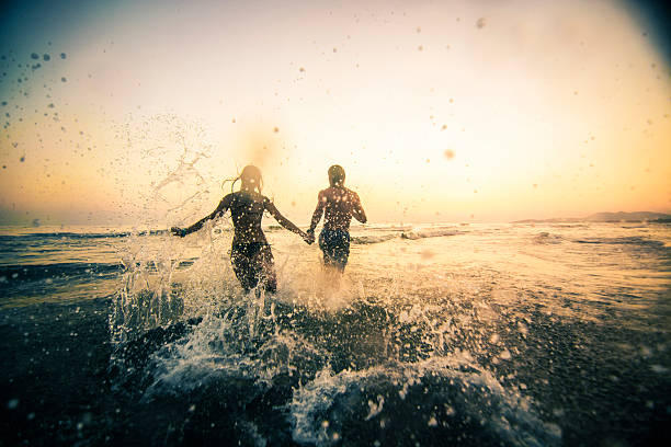 Silhouette of couple in love running in the ocean and holding hands.