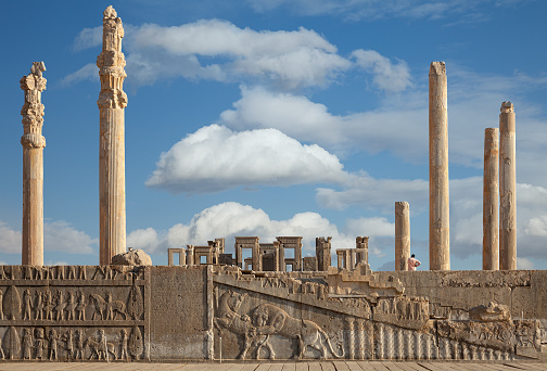 Ruins of Apadana and Tachara Palace behind stairway with bas relief carvings in Persepolis UNESCO World Heritage Site against cloudy blue sky in Shiraz city of Iran.