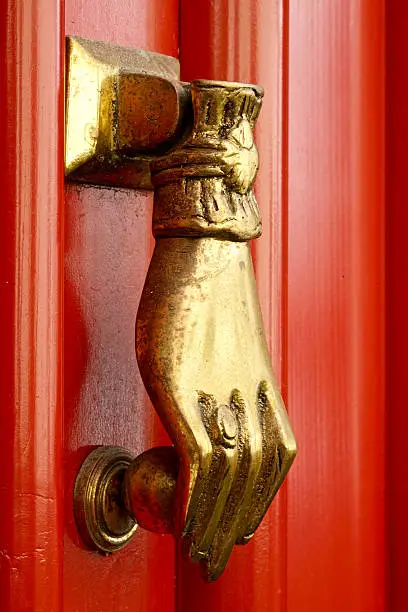 closeup of a brass doorknocker at a bright red door