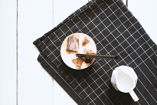 Coffee ice cubes with milk in cup with straw on black tea towel.