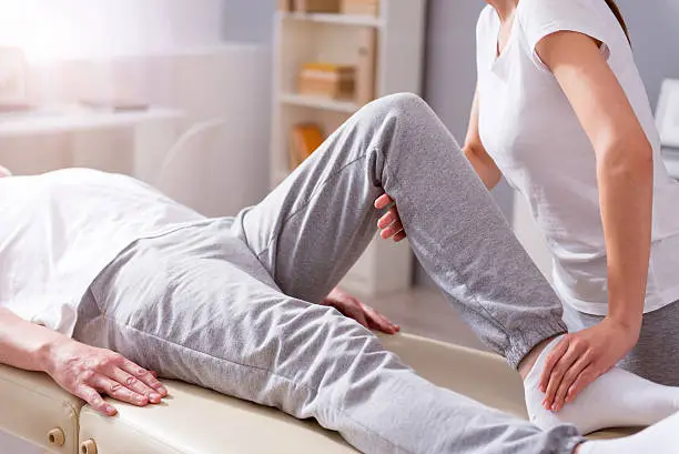 Treatment. Cropped image of male patient lying down with female physiotherapist performing some stretch exercises on mans leg