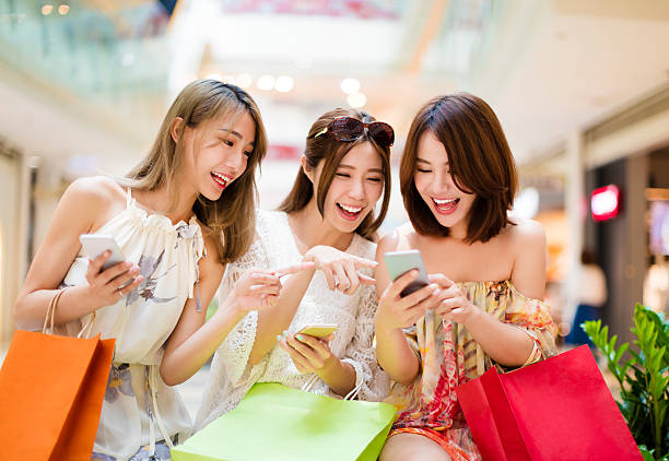 glückliche junge frau aufpassen smartphone in einkaufszentrum - retail shopping talking customer stock-fotos und bilder