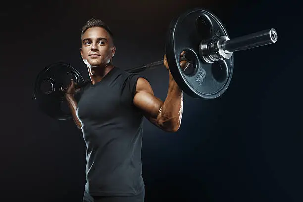 Closeup portrait of professional bodybuilder workout with barbell on black background. Muscular man training squats with barbells over head