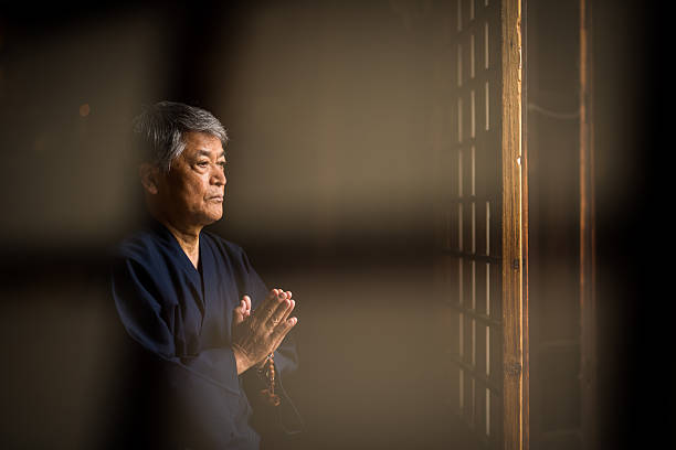 Double exposure of a senior aged Japanese man praying with beads at a Japanese temple
