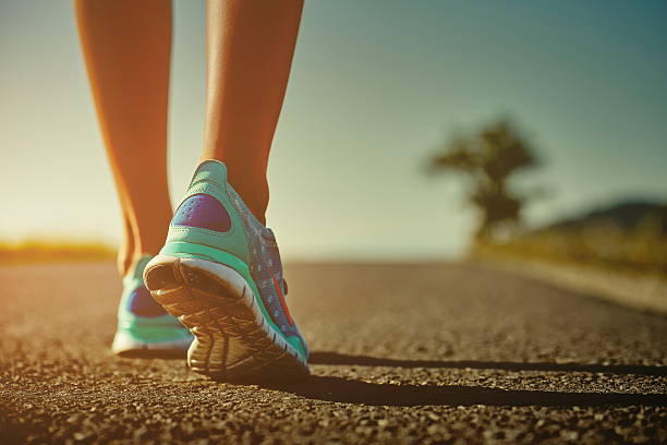 Runner feet and shoes Closeup of female runner shaved feet in running shoes going for a run on the road at sunrise or sunset. Shallow depth of field, toned with instagram like filter, flare effect. running jogging men human leg stock pictures, royalty-free photos & images