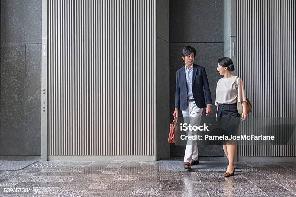 Japanese Businessman And Businesswoman Exiting Elevator In Modern Office Building Stock Photo - Download Image Now