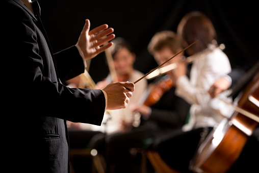 Conductor directing symphony orchestra with performers on background, hands close-up.