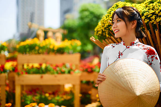 Traditional Clothing. Vietnam. Asian Girl In National Ao Dai Dress Traditional Clothing Of Vietnam, Asia. Beautiful Happy Asian Girl Dressed In National Traditional Ao Dai Dress ( Costume ), Vietnamese Conical Hat ( Non La, Leaf Hat ) In Flower Garden. Culture. vietnamese culture stock pictures, royalty-free photos & images