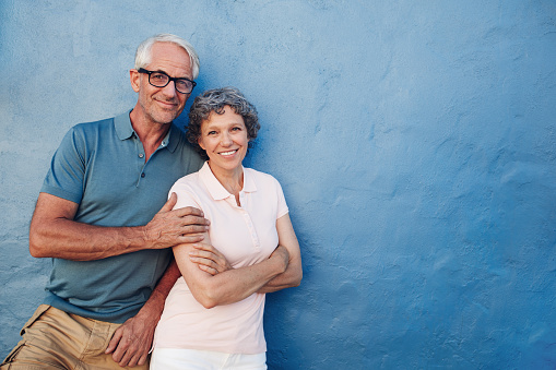 Portrait of happy senior man and woman together against blue background. Middle aged couple looking at camera and smiling with copy space on blue wall.