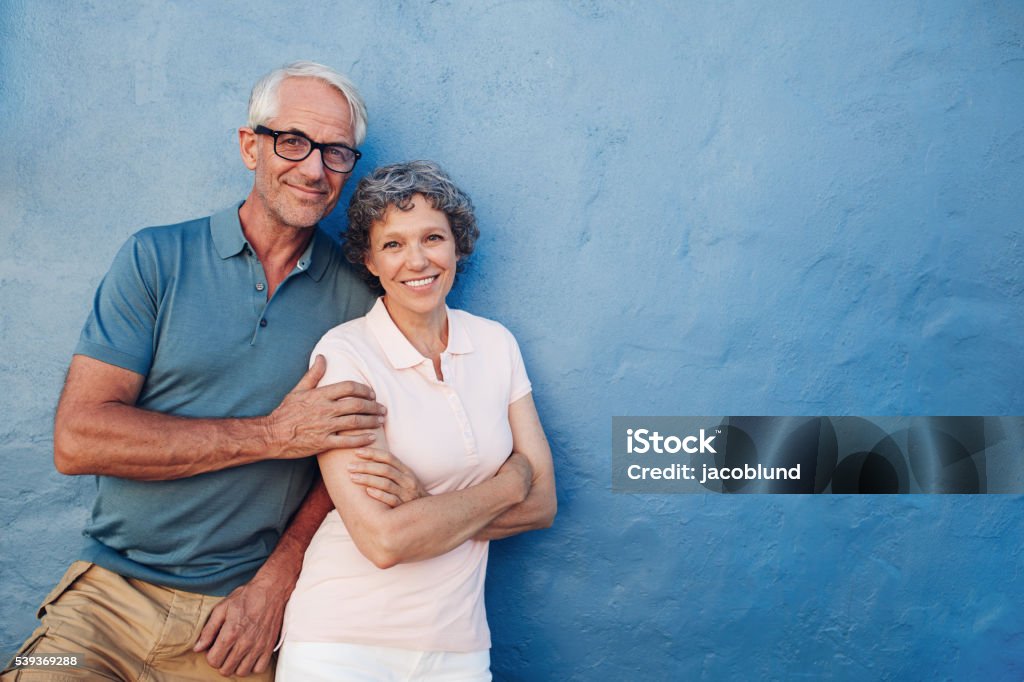 Happy senior man and woman together Portrait of happy senior man and woman together against blue background. Middle aged couple looking at camera and smiling with copy space on blue wall. Couple - Relationship Stock Photo