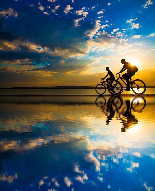 Sporty friends.  bicycle on sunset. Empty Space. Sporty friends on bicycle on sunset. Silhouette couple cyclist go along shoreline coast. Sport in Nature background. Group of people two mountain biker in sunrise with reflection sun in water mountain bike photos stock pictures, royalty-free photos & images