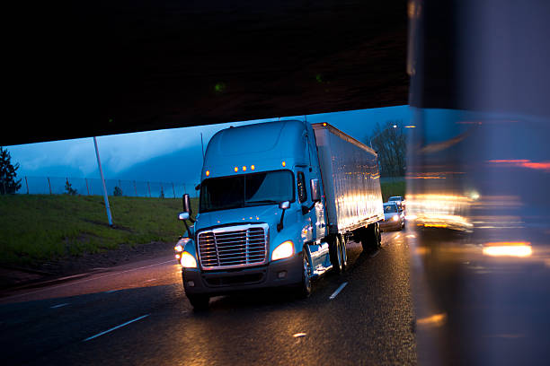 Bright semi truck in raining night lights on highway Blue semi truck in the reflection of the evening headlights lights of car on a wet raining evening road. truck in rain stock pictures, royalty-free photos & images