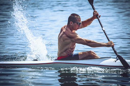 Young muscular man during a kayak sprint training on still water.