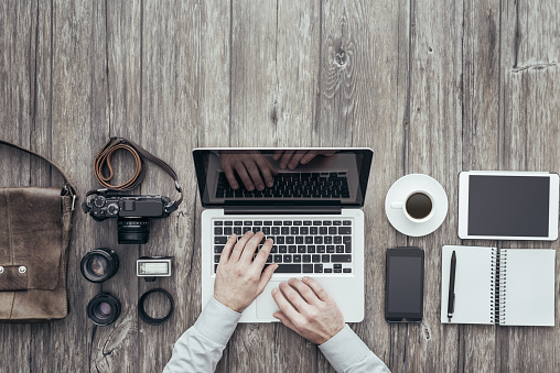 Hipster freelance photography equipment on a wooden desktop and professional photographer working with a laptop, flat lay