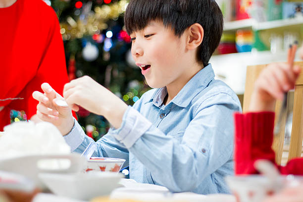 Christmas Prawn Crackers Close up shot of a Chinese boy eating prawn crackers at Christmas dinner with his family. He has a happy expression on his face. eating child cracker asia stock pictures, royalty-free photos & images