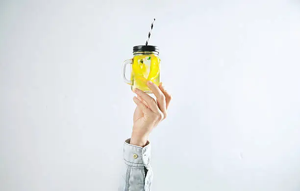 Men hand presents homemade cold lemonade from citrus lemon, sparkling water and ice cubes isolated on white. Refreshment healthy cold drink in summer time