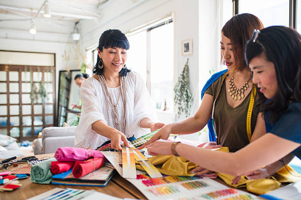 Team of fashion designers looking at colour swatches Three female Japanese fashion designers looking at colour swatches. Kyoto, Japan. May 2016 woman stitching stock pictures, royalty-free photos & images