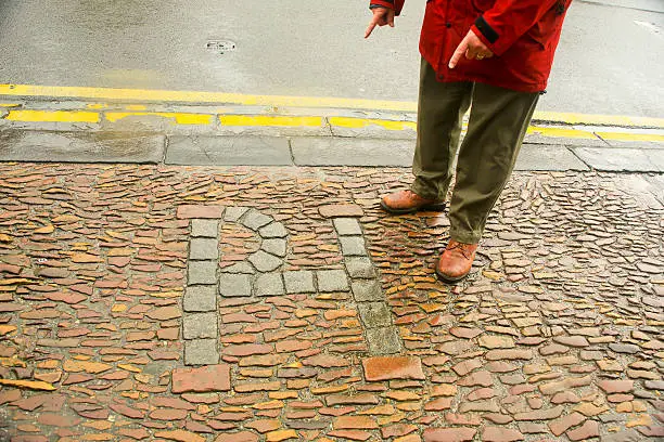 Initials, PH, for Patrick Hamilton who was burned at the stake for heresy May 29, 1541, the first martyr in the Scottish Reformation. A man is pointing at the initials. It is on a cobblestone street in St. Andrews, Scotland, UK. near the University of St. Andrews,