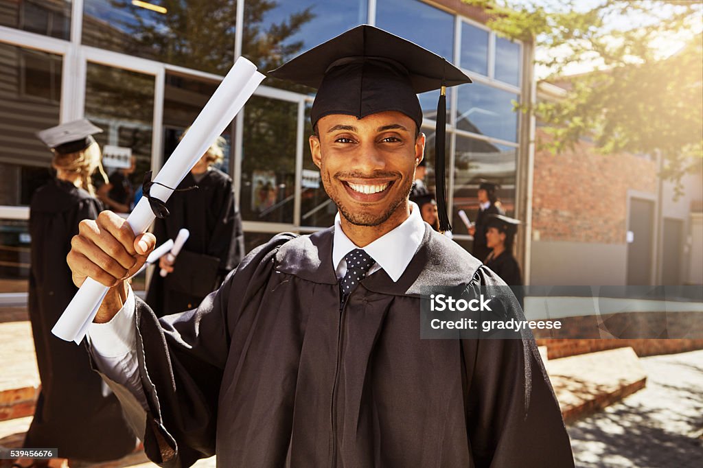 Proud of my scholastic success Portrait of a smiling university student holding his diploma outside on graduation day Diploma Stock Photo