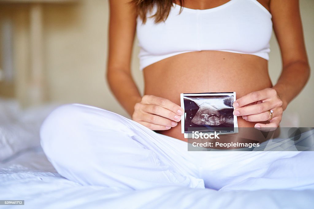 She's excited about her little one Shot of a pregnant woman holding a sonogram picture in front of her belly Pregnant Stock Photo