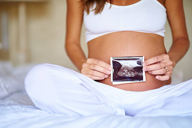 She's excited about her little one Shot of a pregnant woman holding a sonogram picture in front of her belly abdomen photos stock pictures, royalty-free photos & images