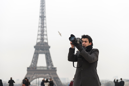 Young man taking pictures in Paris the Eiffel Tower is visible on the background.