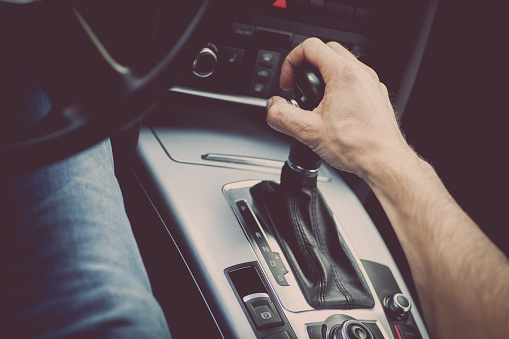 Detail of a hand pulling an automatic gear shifter in a new car.