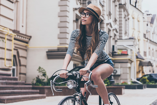 Beautiful young woman riding bicycle along the street and looking curious