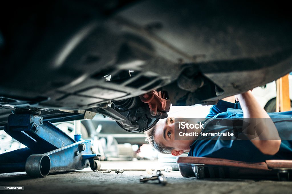 Car Mechanic Working Under Vehicle Low angle view of a mechanic working under a vehicle. Car Stock Photo