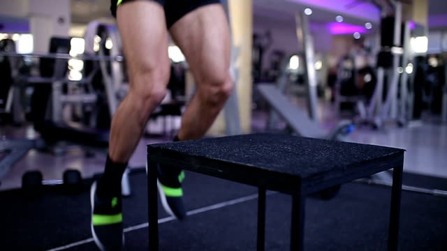 Fit man doing box jumps in gym