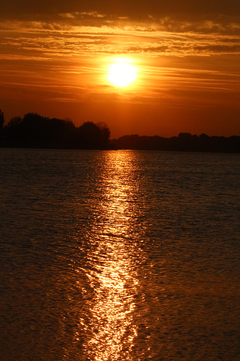 View on an orange full dark sunset reflecting over a water surface of a Lake