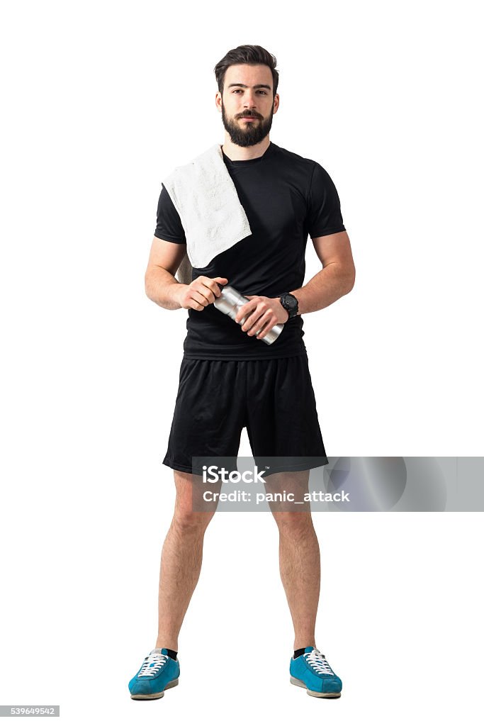 Young confident athlete with towel and bottle looking at camera Young confident athlete with towel and bottle looking at camera. Full body length isolated over white studio background. Men Stock Photo