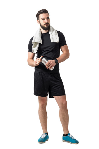 Young bearded male athlete with towel holding plastic water bottle. Full body length isolated over white studio background
