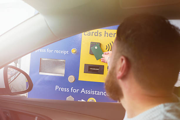 Toll road pay booth A driver is paying the toll charge at a motorway toll booth with his debit card. He is inserting the debit card into the slot to pay the charge.. (Cars and defining toll booth features have been altered) cash in transit vehicle stock pictures, royalty-free photos & images