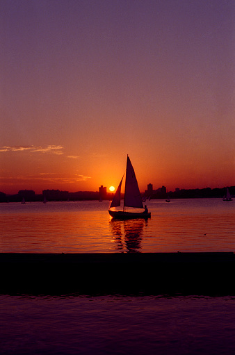 Sailboat on Boston Charles River Basin sailing at Sunset with MIT campus in the background