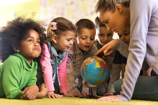 Group of children at preschool examining world globe with their teacher.