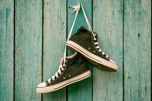 Dark blue sneakers hang on a nail on a blue wooden wall, canvas shoe,toning
