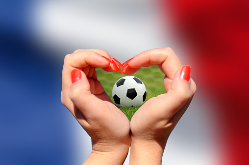 Female hand making a heart shape with soccer ball on France flag background