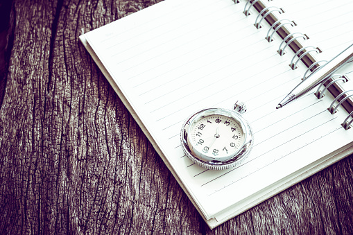 Pocket watch on notebook for notes, On old textured wood. Vintage style.