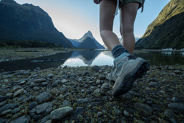 Woman's legs and hiking boots standing on rocky trail Woman's legs and hiking boots standing on rocky trail. Mitre peak and it's reflection on the water on the background. fiordland national park photos stock pictures, royalty-free photos & images